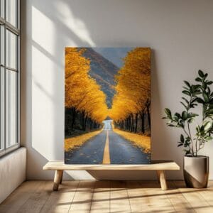 Autumn road landscape print leaning on a wooden bench by a window, featuring yellow fall trees and a long road.
